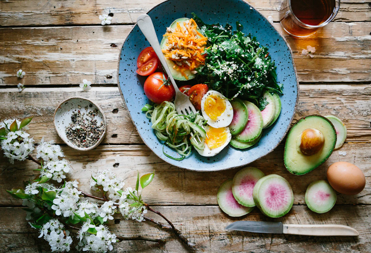 Assiette avec œufs, avocat et légumes posée sur une table en bois