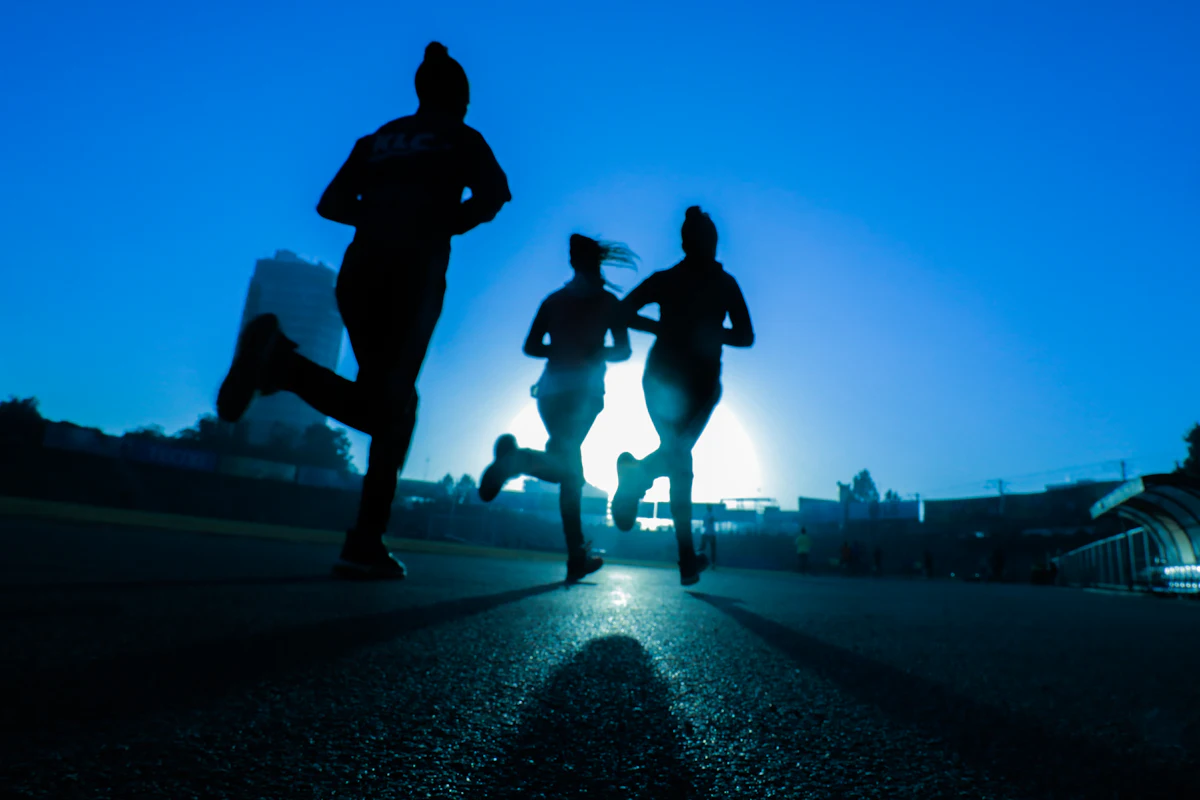 Trois coureurs en silhouette sur une piste, à contre-jour